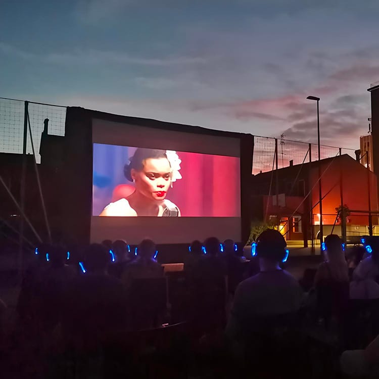 cinema-bologna Υπαίθριος κινηματογράφος στη Μπολόνια στο ηλιοβασίλεμα με το κοινό να φορά ακουστικά