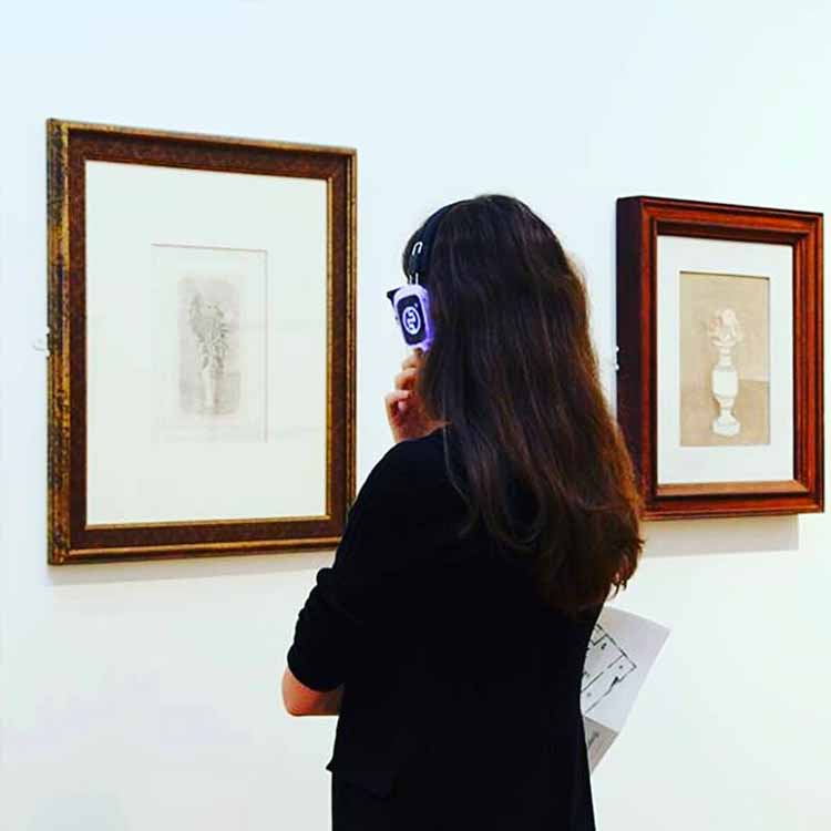 museo-milano Επισκέπτρια μουσείου στο Μιλάνο με ασύρματα ακουστικά μπροστά σε έναν πίνακα