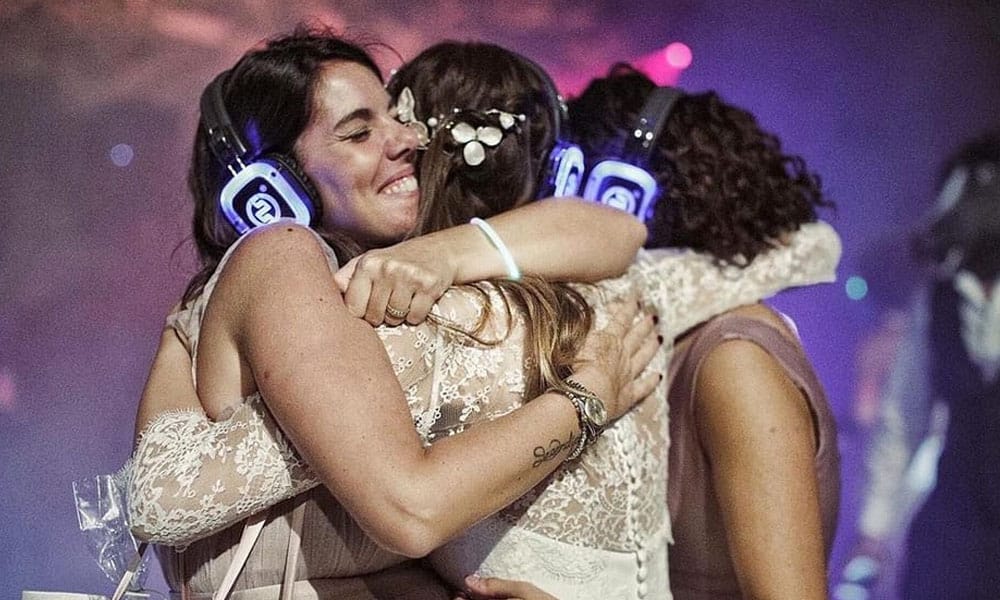 Matrimonio silentdisco Νύφη αγκαλιάζει φίλες φορώντας ακουστικά silent disco